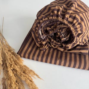 Puede incluir: Sábana bajera de rayas marrones y beige con un patrón ondulado. La sábana está doblada y enrollada.