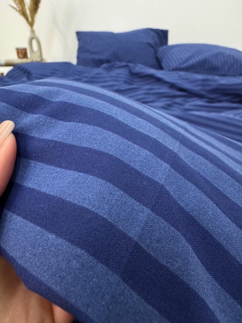 May include: Close-up of a blue striped bedding set. The fabric is soft and textured, with a subtle sheen.