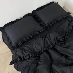 May include: Black bedding set with ruffled edges. The set includes a flat sheet, fitted sheet, and two pillowcases.