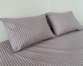 May include: Two striped pillows rest on a matching striped bedsheet. The bedding features a pattern of vertical stripes in shades of gray and white. The pillows are rectangular and appear soft, suggesting a comfortable sleep environment.
