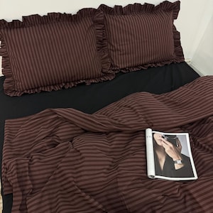 May include: A brown and white striped bedding set with ruffled pillowcases. The bedding is made of a soft, comfortable fabric and is perfect for a bedroom.