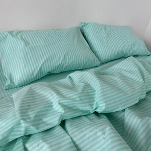 May include: A bedding set featuring two rectangular pillows and a duvet cover, all made from fabric with a repeating pattern of thin, vertical mint green and white stripes. The fabric has a soft, slightly wrinkled texture across the surface.