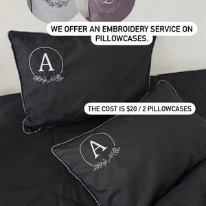 May include: Black pillowcases with white embroidered initials and a floral design. The image shows a close-up of the pillowcases, with the letter "A" embroidered on two pillows. The text "WE OFFER AN EMBROIDERY SERVICE ON PILLOWCASES" is also visible.