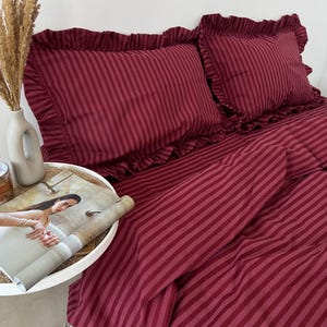 May include: A deep burgundy and dark red striped bedding set featuring two rectangular pillowcases with ruffled edges and a matching duvet cover. The fabric displays a consistent vertical stripe pattern throughout the entire set.