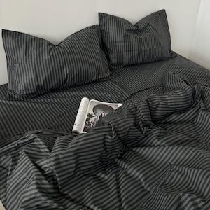 Può includere: Un set di biancheria da letto a righe bianche e nere con una rivista sopra il piumino. La biancheria da letto è realizzata in tessuto morbido e confortevole e presenta un classico motivo a righe.