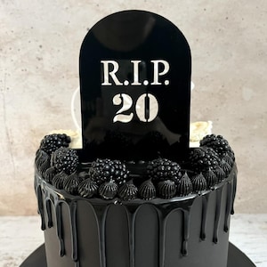 Könnte beinhalten: Schwarzer Kuchen mit schwarzem Frosting und Brombeeren. Ein schwarzer Grabstein-Kuchentopper trägt die Aufschrift "R.I.P. 20".