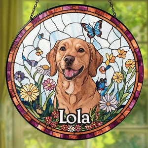 May include: Round stained glass window art featuring a smiling golden Labrador Retriever. The artwork includes colorful flowers, butterflies, and the name "Lola" at the bottom. The window is framed with a decorative border and hangs from a chain.