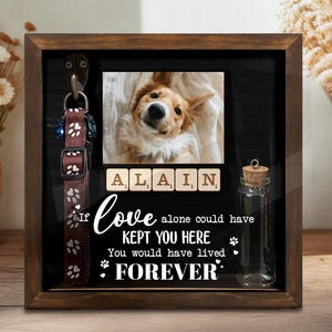May include: A wooden shadow box with a photo of a dog, scrabble tiles spelling "ALAIN", and a brown dog collar. The text reads "If love alone could have kept you here, you would have lived forever."