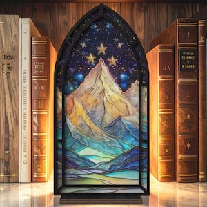 May include: A stained glass panel depicting a mountain range under a starry night sky, framed in black. The panel is set on a marble surface, with a backdrop of antique books on a wooden shelf. The artwork features shades of blue, yellow, and green.
