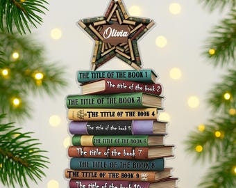 May include: A star-shaped Christmas ornament made of books, with the name "Olivia" on it. Below the star is a stack of books with titles like "The Title of the Book 1" and "The Title of the Book 2". A red and white gingham bow is at the top.