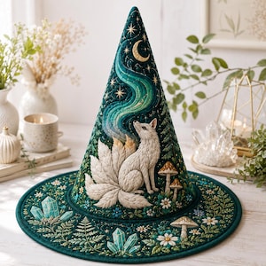 May include: A dark green quilted cone-shaped hat featuring an embroidered white multi-tailed fox looking up at a crescent moon and swirling teal aurora. The design includes gold stars, mushrooms, small white flowers, green ferns, and teal crystals.