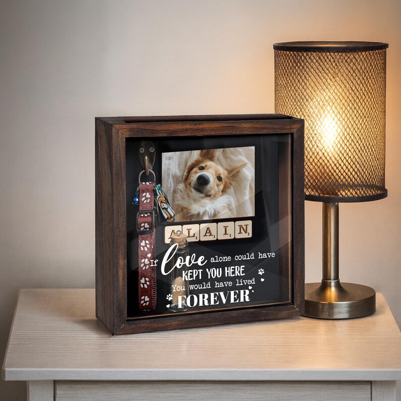 May include: A wooden shadow box with a glass front, displaying a photo of a dog, scrabble tiles spelling "ALAIN", and the text "If love alone could have kept you here, you would have lived forever." A dog collar and leash hang inside.