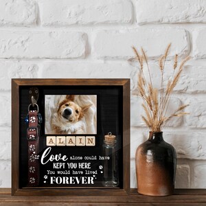 May include: A framed pet memorial with a photo of a dog, a collar, and a small glass bottle. The text reads "If love alone could have kept you here, you would have lived forever." The dog's name, Alain, is spelled out in Scrabble tiles.