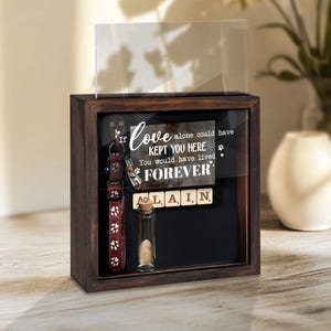 May include: A dark wooden shadow box with a clear glass front. Inside, a pet collar, a small glass vial, and a sign that reads "If love alone could have kept you here, you would have lived forever."