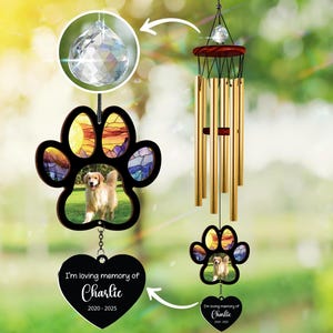May include: A memorial wind chime with a paw print design and a photo of a golden retriever. The paw print has a stained glass effect with sunset colours. A heart-shaped pendant reads "I'm loving memory of Charlie 2020-2025".