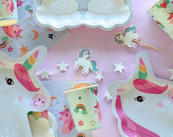 May include: A collection of unicorn-themed party supplies, including paper plates, cups, napkins, and cupcake toppers. The plates are shaped like unicorns and rainbows. The color palette includes pink, white, and pastel rainbow colors. Star-shaped confetti is scattered around the items.