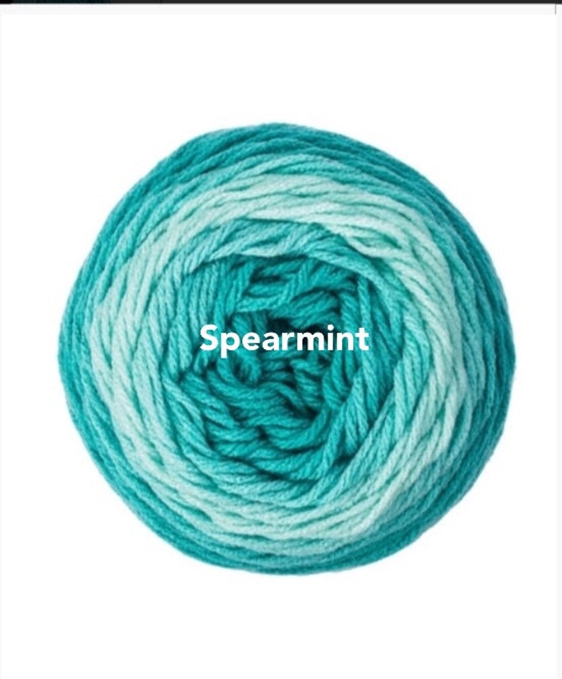May include: A ball of Spearmint-colored yarn, featuring a gradient of teal and light blue hues. The yarn is tightly wound, creating a circular shape. The word "Spearmint" is printed in white across the center of the yarn ball.