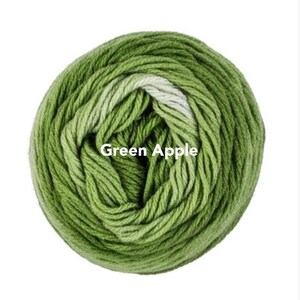May include: A ball of Green Apple yarn, a blend of green shades, is tightly wound. The yarn is labeled with the text "Green Apple". This yarn is suitable for knitting and crochet projects.