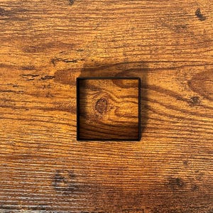May include: A black square frame on a brown wood background.