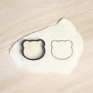 May include: Two bear-shaped cookie cutters, one black and one white, on a white surface.
