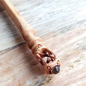 Op de afbeelding: Een handgesneden houten toverstaf met ingewikkelde details. De toverstaf heeft een gesneden handvat met een edelsteen aan de punt. De toverstaf is lichtbruin en heeft de tekst "Yevhen Shevchenko".
