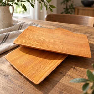 Puede incluir: Dos bandejas de servicio rectangulares de madera con un acabado marrón claro y patrones de veta de madera natural visibles. Las bandejas están apiladas ligeramente desplazadas, con esquinas redondeadas y una superficie plana y pulida.