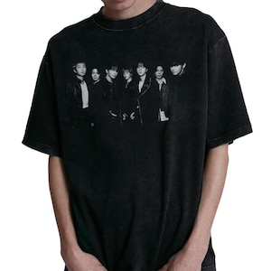 May include: Black t-shirt featuring a grayscale image of seven people. The image is centered on the front of the shirt. The shirt has a crew neck and short sleeves. The fabric appears to be slightly faded.