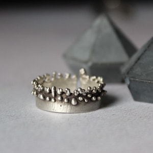 May include: A silver ring with a textured band and a raised design of small, round bumps.