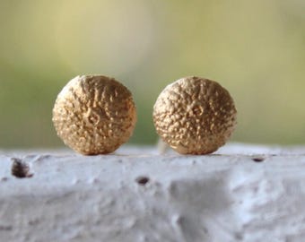 May include: A pair of gold-toned stud earrings with a textured, spherical design.