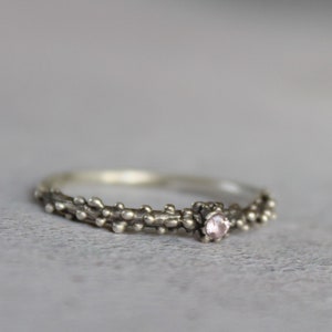 May include: A silver ring with a delicate, textured band and a small pink gemstone in the centre.