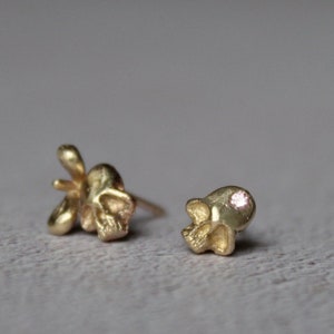 Peut inclure: Deux boucles d'oreilles en forme de cr&acirc;ne en or, l'une avec une petite pierre pr&eacute;cieuse rose dans l'orbite.