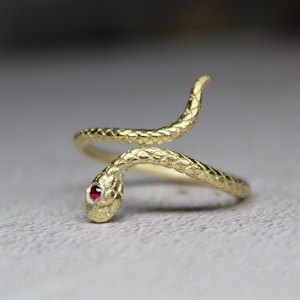Peut inclure: Une bague en or en forme de serpent avec un œil en pierre rouge. Le serpent est enroulé autour de la bande de la bague.