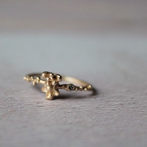 May include: A gold ring with a textured, organic design featuring a small green gemstone. The ring is delicate and has a unique, nature-inspired look.