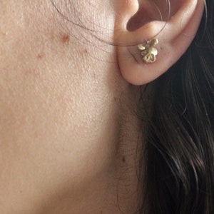 Peut inclure: Gros plan sur l'oreille d'une personne avec une petite boucle d'oreille en forme de fleur dor&eacute;e.