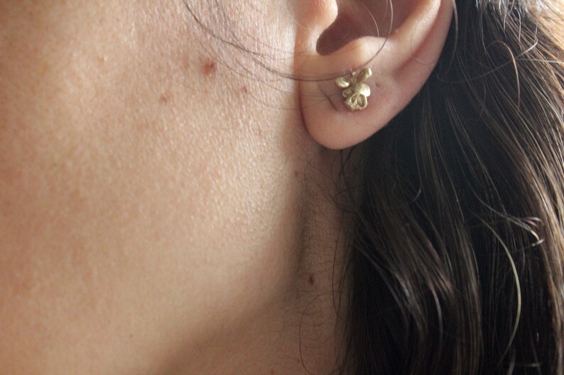 Peut inclure: Gros plan sur l'oreille d'une personne avec une petite boucle d'oreille en forme de fleur dor&eacute;e.