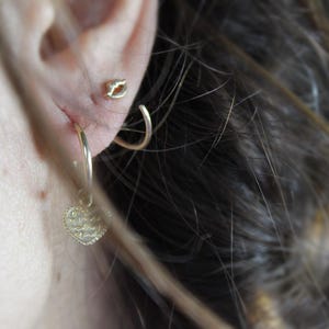 May include: Gold hoop earrings with a small heart charm dangling from one earring. The heart charm is covered in small, sparkling stones.