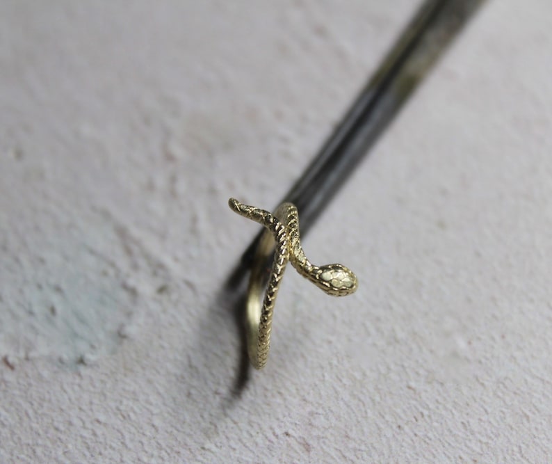 May include: A gold snake ring with a textured finish. The snake is coiled around the ring band.