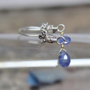 May include: Silver hoop earrings with a skull charm and a teardrop-shaped blue gemstone dangle.
