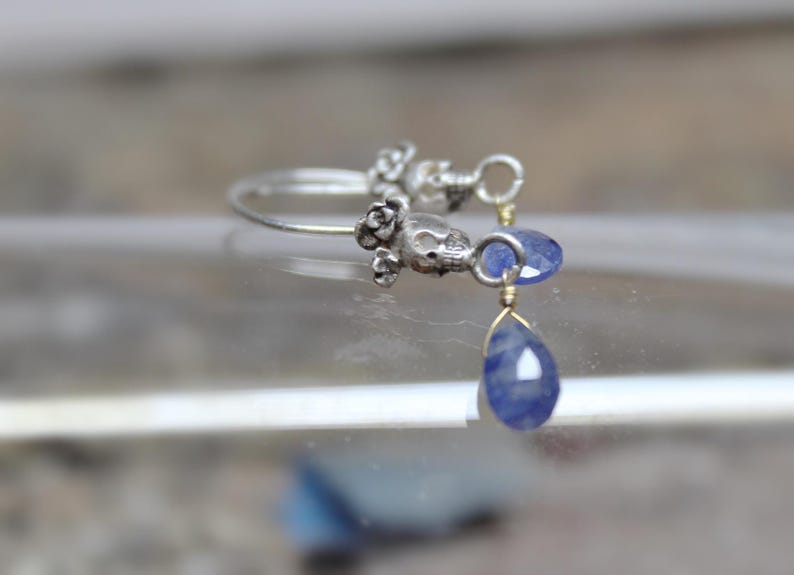 May include: Silver hoop earrings with a skull charm and a teardrop-shaped blue gemstone dangle.