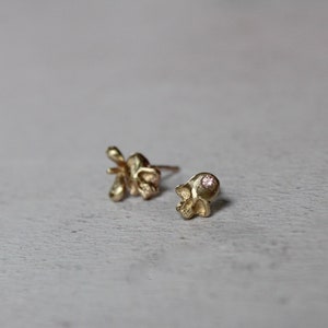 Peut inclure: Une paire de boucles d'oreilles en or, l'une en forme de fleur et l'autre en forme de cr&acirc;ne. La boucle d'oreille en forme de cr&acirc;ne a une petite pierre pr&eacute;cieuse rose dans l'orbite de l'&oelig;il.