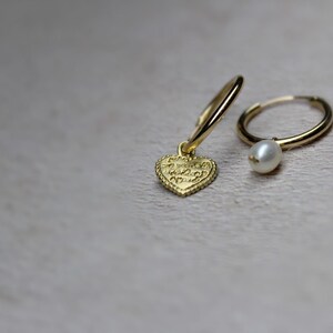 May include: A pair of gold hoop earrings, one with a small gold heart charm and the other with a white pearl charm.