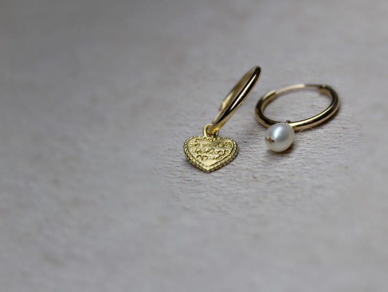 May include: A pair of gold hoop earrings, one with a small gold heart charm and the other with a white pearl charm.