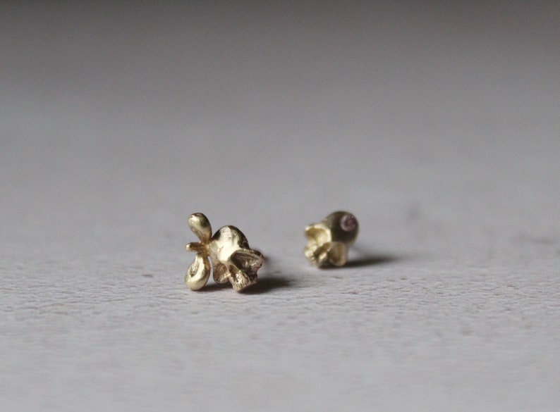 Peut inclure: Une paire de boucles d'oreilles en forme de cr&acirc;ne en or. L'une des boucles d'oreilles a une petite pierre rose dans l'orbite de l'&oelig;il.