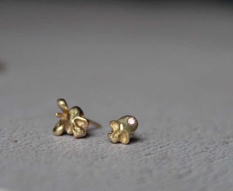 Peut inclure: Deux boucles d'oreilles en forme de cr&acirc;ne en or, l'une avec une petite pierre pr&eacute;cieuse rose dans l'orbite.
