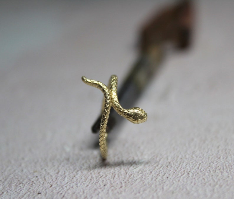 May include: A gold-colored snake ring with a textured surface. The snake is curled up with its head facing forward.