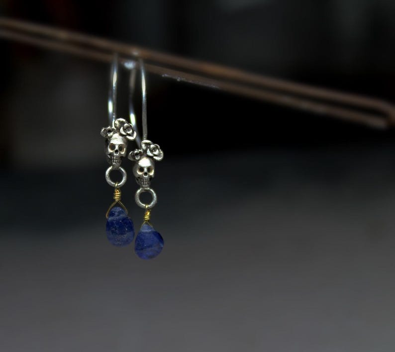 May include: A pair of silver hoop earrings with a skull charm and a blue gemstone dangle.
