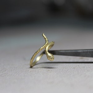 May include: A gold snake ring with a textured finish. The snake is coiled around the ring band and the head is facing forward.