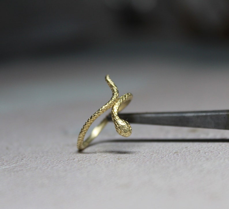 May include: A gold snake ring with a textured finish. The snake is coiled around the ring band and the head is facing forward.