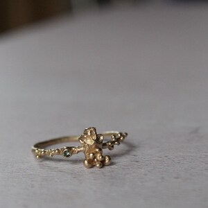 May include: A gold ring with a textured design resembling a branch with small green gemstones.