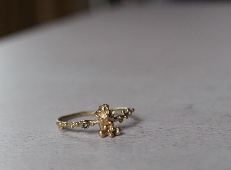 May include: A gold ring with a textured design resembling a branch with small green gemstones.